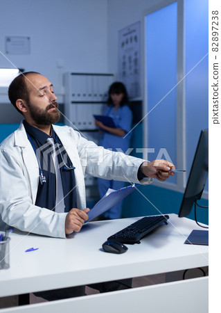 Focused doctor pointing at computer for analysis work at night Focused doctor pointing at computer for analysis work at night 82897238