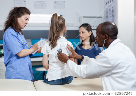African american pediatrician doctor examining lungs of young children 82897245