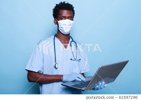 Healthcare assistant with laptop in hand wearing face mask Healthcare assistant with laptop in hand wearing face mask 82897296