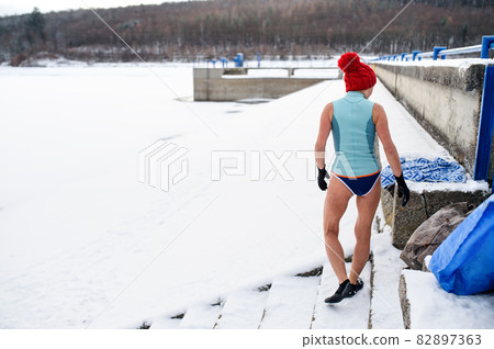 Rear view of active senior woman in swimsuit getting ready for exercise outdoors in winter, cold therapy concept. Rear view of active senior woman in swimsuit getting ready for exercise outdoors in winter, cold therapy concept. 82897363