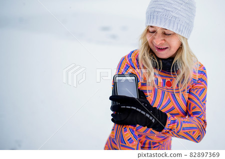 Active senior woman runner adjusting smartphone, attached to arm, for exercising outdoors in snowy winte. Active senior woman runner adjusting smartphone, attached to arm, for exercising outdoors in snowy winte. 82897369