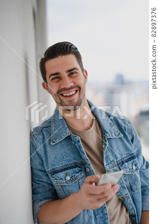 Portrait of young caucasian man with smartphone standing on balcony, looking at camera. Portrait of young caucasian man with smartphone standing on balcony, looking at camera. 82897376