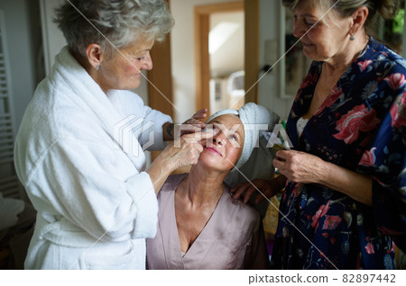 Happy senior women friends in bathrobes applying anti wrinkle patches indoors at home, selfcare concept. Happy senior women friends in bathrobes applying anti wrinkle patches indoors at home, selfcare concept. 82897442