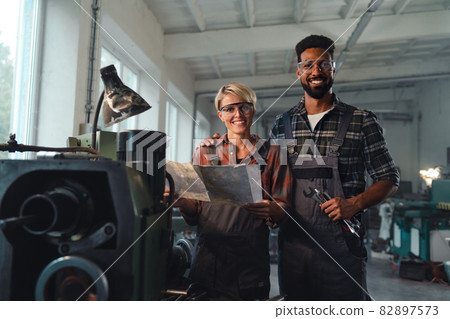 Portrait of young biracial industrial colleagues working indoors in metal workshop, smiling and looking at camera. 82897573