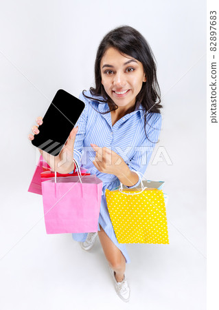 Close-up of happy smiling young girl with lots of shopping bags, colorful bright packages isolated over white background. Close-up of happy smiling young girl with lots of shopping bags, colorful bright packages isolated over white background. 82897683