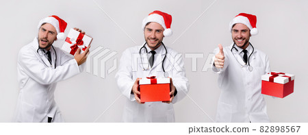Young handsome doctor in white uniforme and Santa Claus hat standing in studio on white background smile and finger in camera 82898567