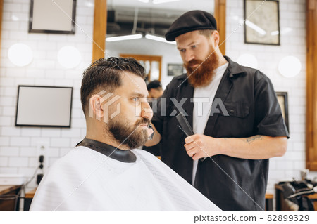 Man getting haircut at the barbershop. Professional barber at work process. Beauty, selfcare, style, fashion, healthcare and male cosmetics concept. Man getting haircut at the barbershop. Professional barber at work process. Beauty, selfcare, style, fashion, healthcare and male cosmetics concept. 82899329