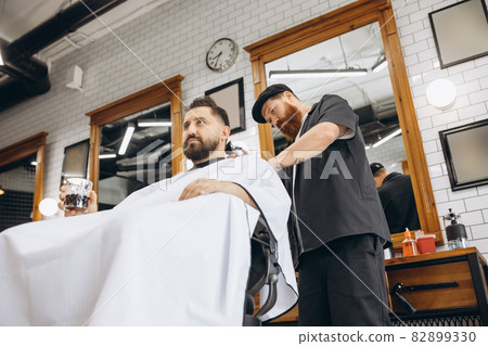 Two handsome men at barbershop. Stylish red-bearded barber and client during haircut process. Beauty, healthcare and male cosmetics concept. Two handsome men at barbershop. Stylish red-bearded barber and client during haircut process. Beauty, healthcare and male cosmetics concept. 82899330