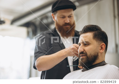 Man getting haircut at the barbershop. Professional barber at work process. Beauty, selfcare, style, fashion, healthcare and male cosmetics concept. 82899419
