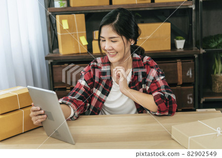 Asian woman startup small business at home office. Online seller entrepreneur young asian woman use tablet checking online order. Woman using tablet check stock goods supply delivery package shipping 82902549