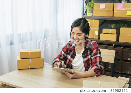 Asian woman startup small business at home office. Online seller entrepreneur young asian woman use tablet checking online order. Woman using tablet check stock goods supply delivery package shipping 82902551