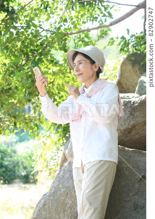 Senior woman smart phone knee-up relaxing in the nature of trees and huge rocks 82902747