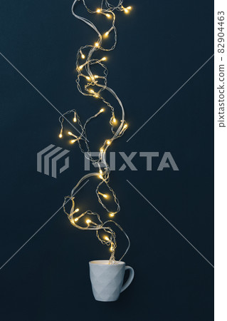 Garland with yellow bulbs on a black background and a cup of hot drink. Flat lay. 82904463
