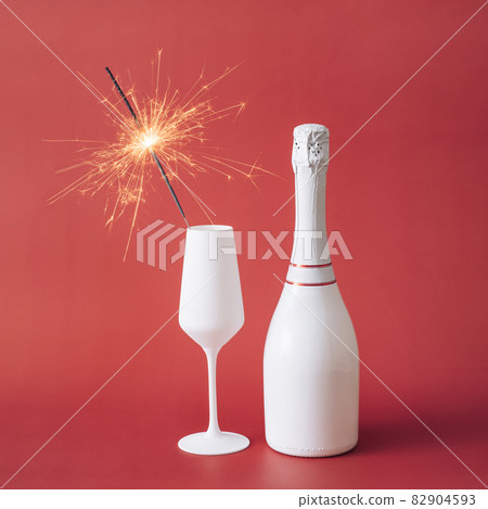 Sparkler in white flute next to a unlabeled bottle of champagne Sparkler in white flute next to a unlabeled bottle of champagne 82904593