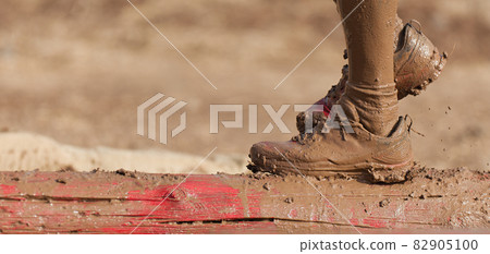 Mud race runners. Participant walking on the tree trunk, catches balance above the pit full of water Mud race runners. Participant walking on the tree trunk, catches balance above the pit full of water 82905100