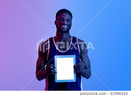 Smiling black sportsman showing digital tablet with blank screen in neon light, mockup for app or website Smiling black sportsman showing digital tablet with blank screen in neon light, mockup for app or website 82906826