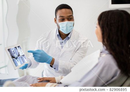 Black Stomatologist Showing Digital Tablet With Teeth Xray Picture To Female Patient 82906895