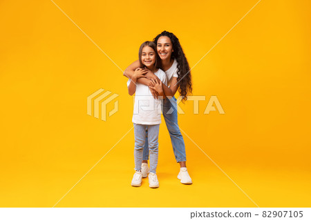 Middle-Eastern Mother Hugging Her Lovely Little Daughter On Yellow Background 82907105