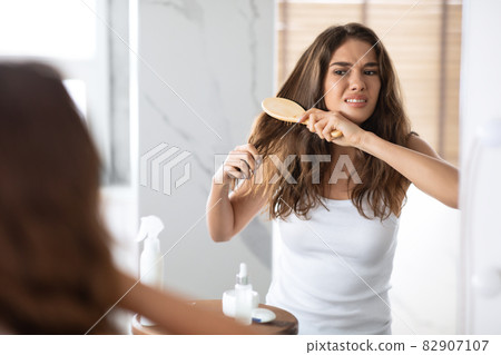 Desperate Woman Brushing Dry Tangled Hair With Hairbrush At Home 82907107