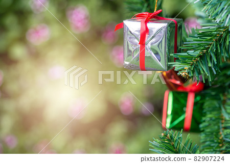 Close up of a wrapped gift box hanging on a branch of Christmas tree. Gift or present is an item given to someone without the expectation of payment or anything in return. 82907224