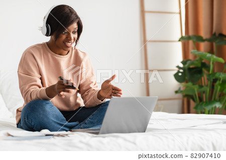 African American Female Video Calling Using Laptop Wearing Earphones Indoors 82907410