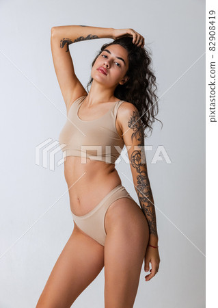Cropped portrait of beautiful tender woman in beige inner wear isolated over gray background Cropped portrait of beautiful tender woman in beige inner wear isolated over gray background 82908419