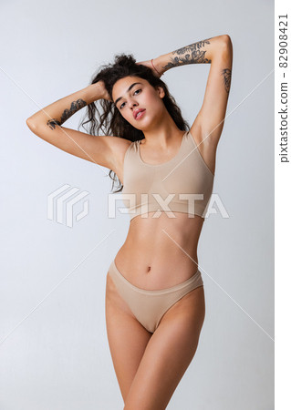 Cropped portrait of beautiful tender woman in beige inner wear isolated over gray background 82908421
