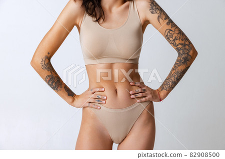 Cropped portrait of tender slim tanned female body in beige inner wear isolated over gray background. Sportive body 82908500