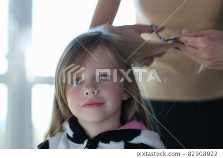 Woman scissors hair of cute blonde little girl closeup 82908922
