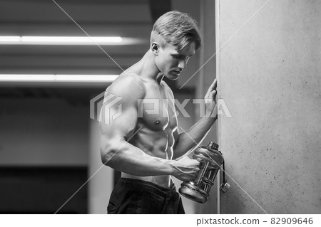 Young athletic man pumping up muscles in the gym at workout. Sport and health care concept background 82909646