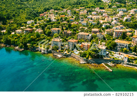 Beautiful villas near the coast of rocky beach in a small town Lovran, Croatia. Arial view of Lungomare sea walkway with transparent water. Beautiful villas near the coast of rocky beach in a small town Lovran, Croatia. Arial view of Lungomare sea walkway with transparent water. 82910215