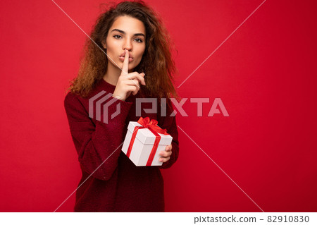 Shot of pretty young brunette curly woman isolated over red background wall wearing red sweater 82910830