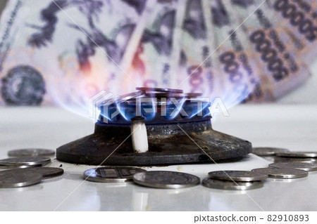 Burning gas stove burner and Uzbek money - sum banknotes. Pay for natural gas, bill, tariff. Growing tariffs for gas. Pile of coins and burning fire gas stove hob and money 82910893