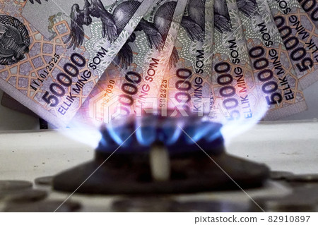Burning gas stove burner and Uzbek money - sum banknotes. Pay for natural gas, bill, tariff. Growing tariffs for gas. Pile of coins and burning fire gas stove hob and money 82910897