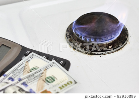 Burning gas stove burner, calculator and US dollar banknotes. Pay for natural gas, bill, tariff. Pile of coins and burning fire gas stove hob and money. Calculating gas tariff or cost 82910899