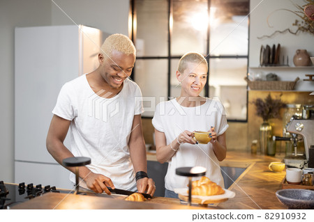 Multiracial couple drinking from cups at kitchen 82910932