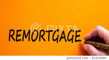 Remortgage symbol. Businessman writing the word 'remortgage', isolated on beautiful orange background. Business and remortgage concept, copy space. Remortgage symbol. Businessman writing the word 'remortgage', isolated on beautiful orange background. Business and remortgage concept, copy space. 82910995