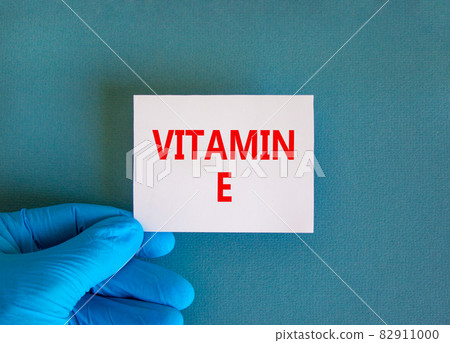 Vitamin E symbol. White note with words Vitamin E, beautiful blue background, doctor hand in blue glove. Medical, vitamin E concept. Vitamin E symbol. White note with words Vitamin E, beautiful blue background, doctor hand in blue glove. Medical, vitamin E concept. 82911000