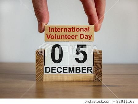 Male hand puts a block with the inscription 'International volunteer Day' on cubes with the date december 05. Beautiful wooden table, white background, copy space. 82911162