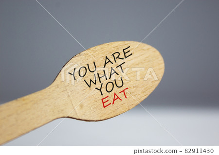You are what you eat symbol. Wooden spoon on white background. Beautiful warm sunlight. Words 'You are what you eat'. Beautiful white background. Healthy eating concept. Copy space. You are what you eat symbol. Wooden spoon on white background. Beautiful warm sunlight. Words 'You are what you eat'. Beautiful white background. Healthy eating concept. Copy space. 82911430