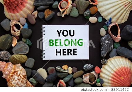 Inclusion and belonging symbol. Words you belong here on a beautiful white note, black background. Sea stones and seashells. Business, inclusion, belonging and you belong here concept. 82911432