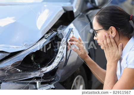 Woman driver looks at wrecked car closeup Woman driver looks at wrecked car closeup 82911567
