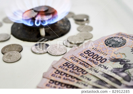 Burning gas stove burner and Uzbek money - sum banknotes. Pay for natural gas, bill, tariff. Growing tariffs for gas. Pile of coins and burning fire gas stove hob and money 82912285