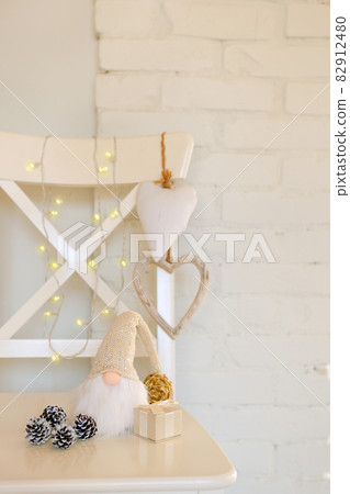 Cute gnome with long beard. white cristmas dwarf near hearts, pine cones and warm lights and brick wall Cute gnome with long beard. white cristmas dwarf near hearts, pine cones and warm lights and brick wall 82912480