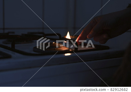 Woman trying to turn on gas with a match flame. Female hand trying to turn on old gas stove. No gas, Winter and cold period concepts. Lack of gas in the pipeline Woman trying to turn on gas with a match flame. Female hand trying to turn on old gas stove. No gas, Winter and cold period concepts. Lack of gas in the pipeline 82912682