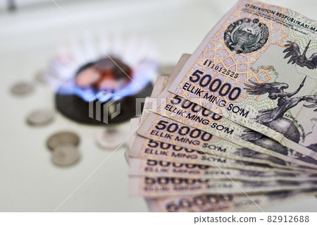 Burning gas stove burner and Uzbek money - sum banknotes. Pay for natural gas, bill, tariff. Growing tariffs for gas. Pile of coins and burning fire gas stove hob and money 82912688