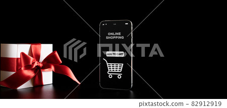 Season sale. Internet online shopping app on mobile phone, white gift box with red ribbon isolated on black background in Black Friday background. Shopping gift concept. Season sale. Internet online shopping app on mobile phone, white gift box with red ribbon isolated on black background in Black Friday background. Shopping gift concept. 82912919