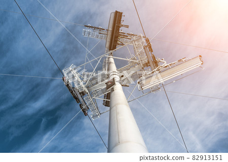 Bottom up overhead view of big metal pillar with Ski lift ropeway crossroad intersection on hilghland alpine mountain winter resort on sunny day. Ski chairlift cable way with people enjoy skiing 82913151
