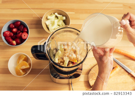 Hands of female pouring milk into blender with chopped ingredients Hands of female pouring milk into blender with chopped ingredients 82913343