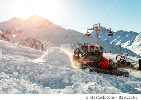 Red modern snowcat ratrack with snowplow snow grooming machine preparing ski slope piste hill at alpine skiing winter resort Ischgl in Austria. Heavy machinery mountain equipment track vehicle 82913563